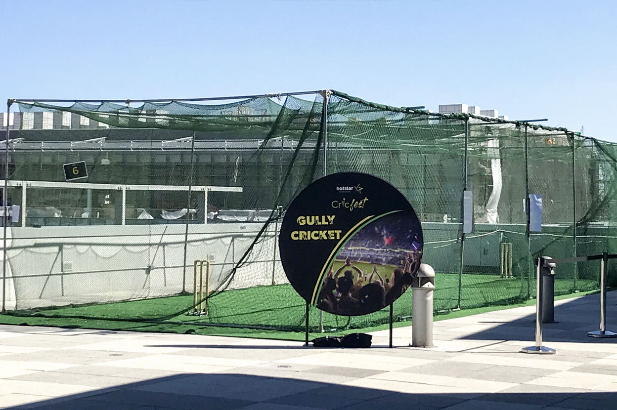 Two purple backdrops with wicketkeepers printed on them behind astroturf mats with cricket wickets.