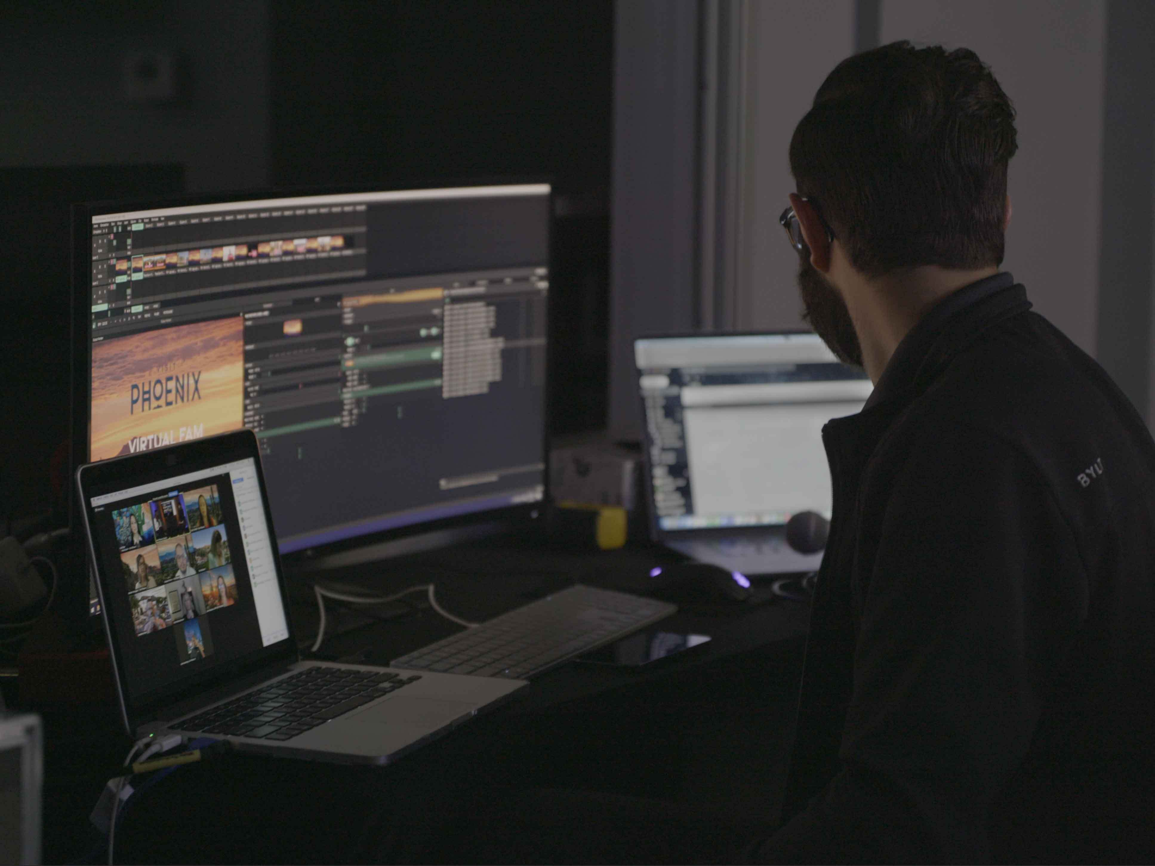 Man sits at a desk with multiple computers, monitoring a livestream and cueing graphics.